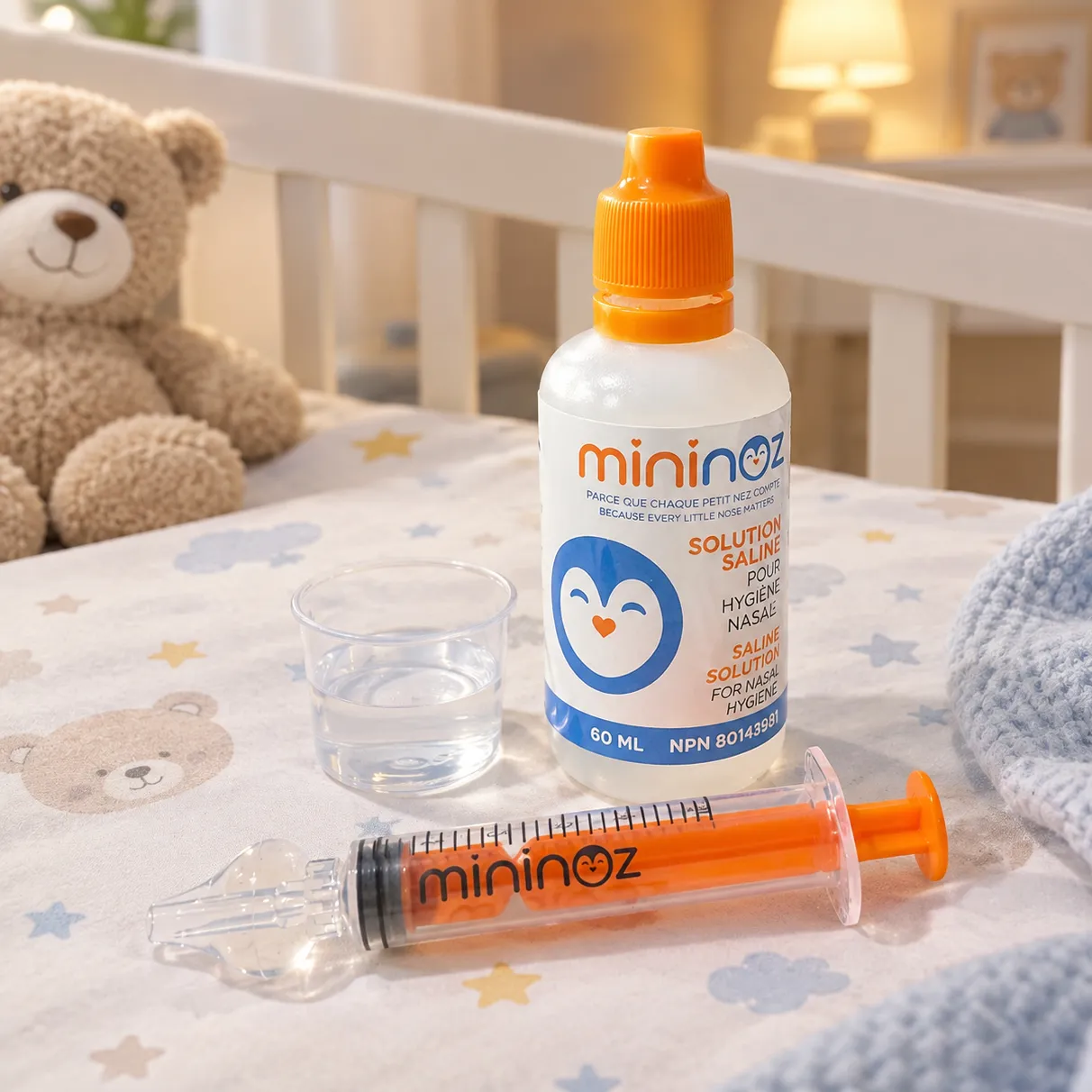 Flacon de solution saline et seringue Mininoz posés sur une couverture d'enfant, près d'un ourson